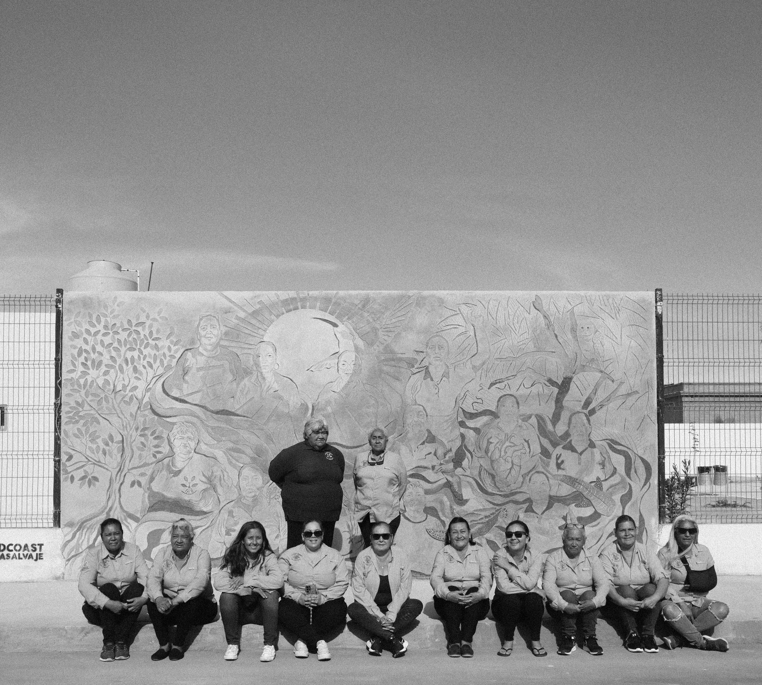 Las Guardianas del Conchalito posan juntas frente a un mural comunitario en La Paz, Baja California Sur.